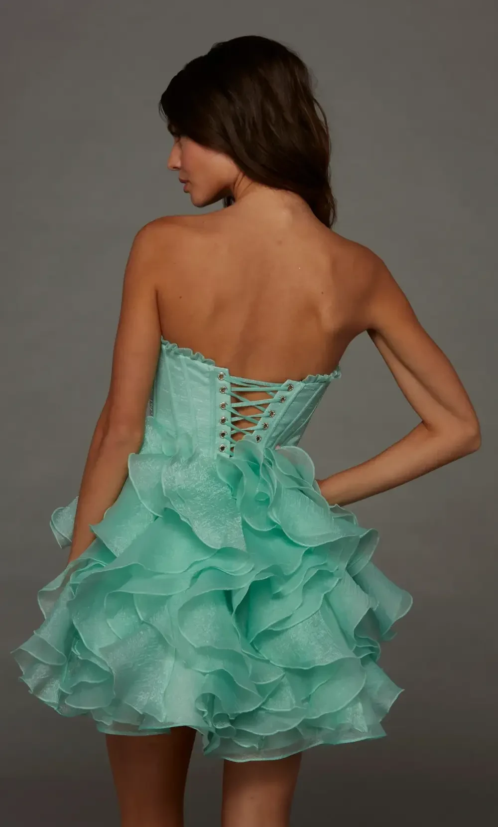 A young woman in a light teal, ruffled strapless dress, posing gracefully against a gray background.