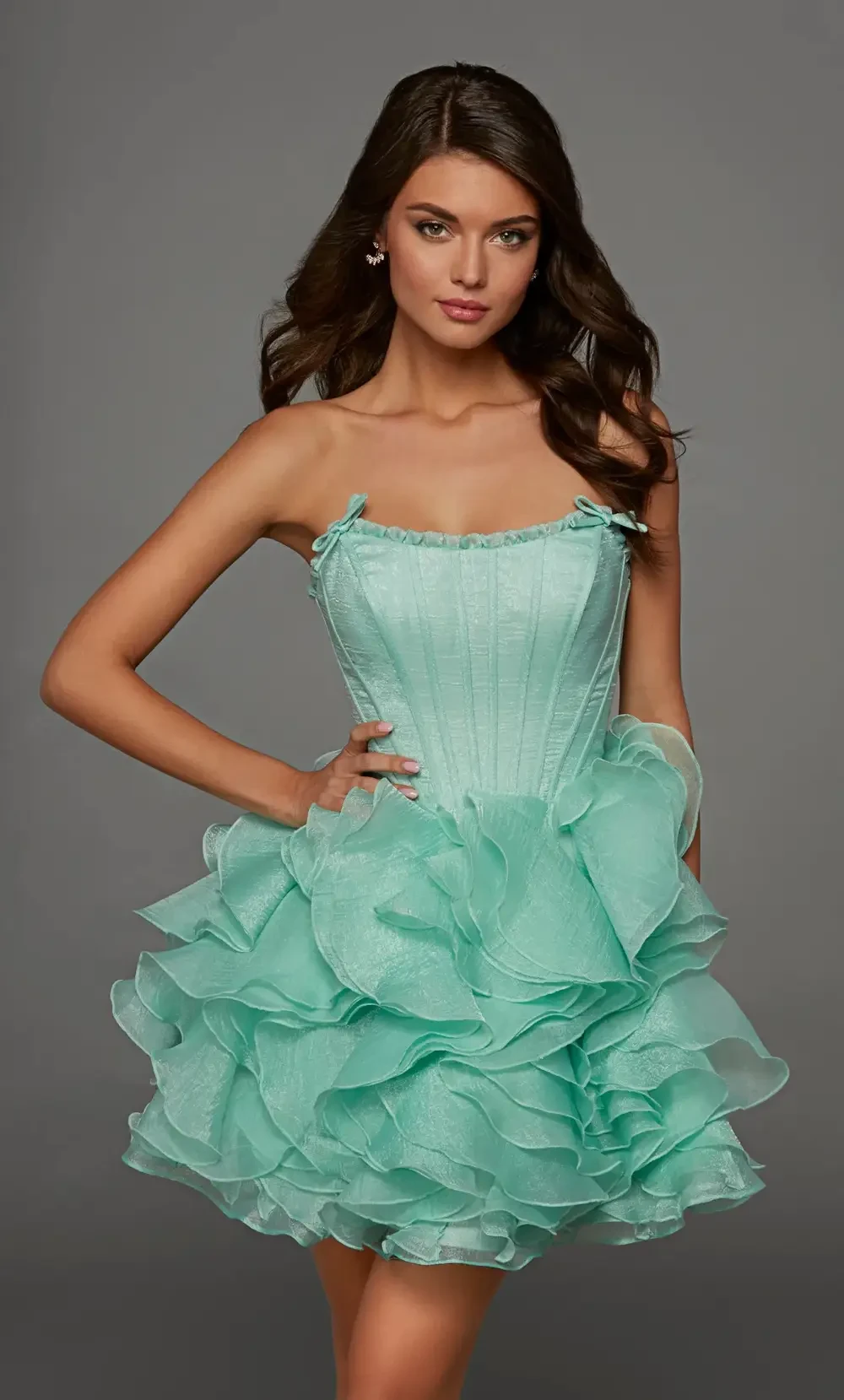 A young woman in a light teal, ruffled strapless dress, posing gracefully against a gray background.